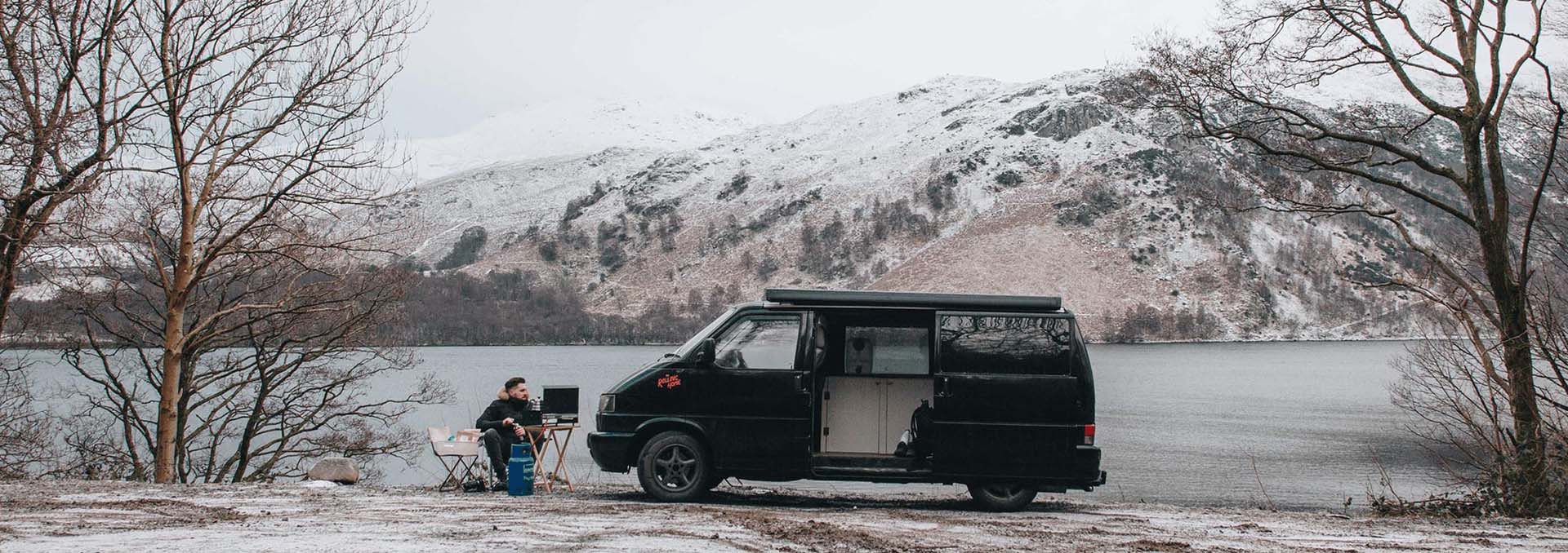 A VW T4 parked up by a snowy take, with a man camping outside