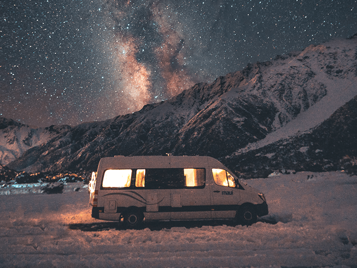 A Mercedes Sprinter parked in a snowy mountainscape with lights on inside